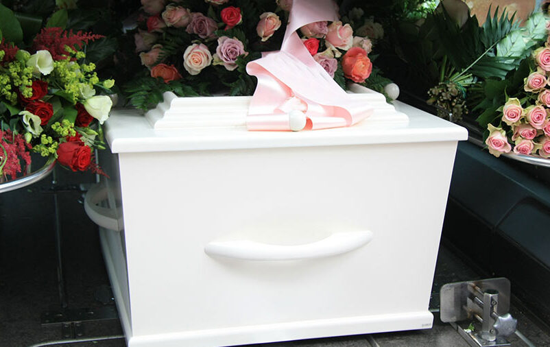 É possível ver caixão envolto em flores. Inicia-se o processo de como é feito o traslado de corpos.