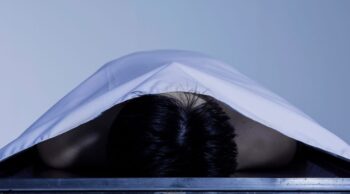 Entenda a diferença entre decomposição e putrefação! Corpo coberto por lençol branco em necrotério ilustra a decomposição e putrefação.