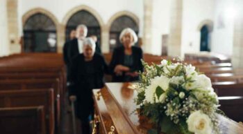 Remoção de corpos: entenda como funciona o procedimento e as normas legais Pessoas em funeral de terno e vestido preto com flores e remoção de corpos