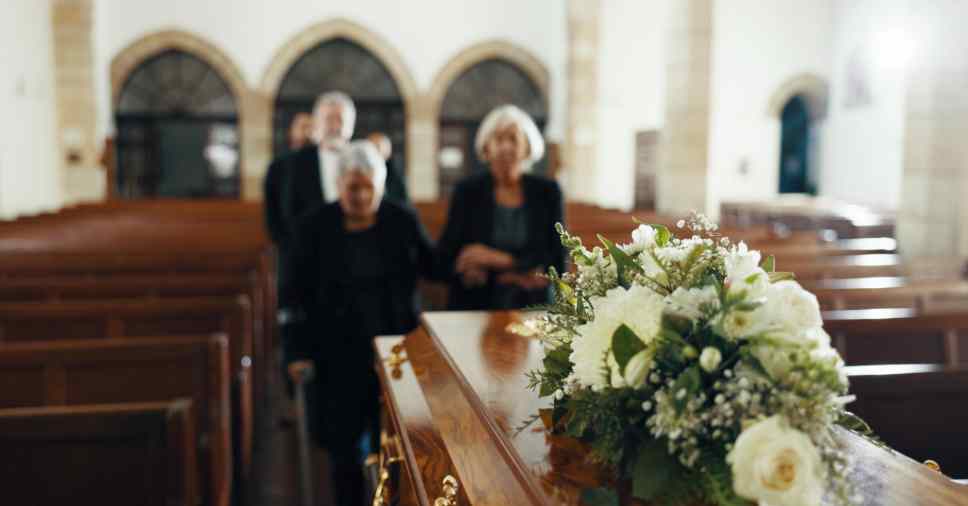 Pessoas em funeral de terno e vestido preto com flores e remoção de corpos