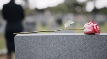 Planeamento funerário e logistica de traslado com a Central Traslado. Rosa pousada sobre uma lápide com uma figura de preto, ilustrando o apoio em logistica de traslado.